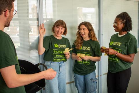 A group of 3 women in Anthony Nolan tshirts drawing raffle tickets from a bucket held by a man in an Anthony Nolan tshirt