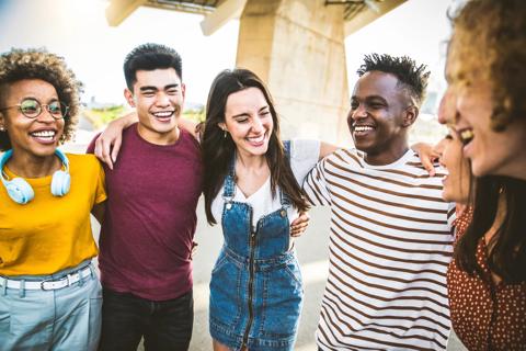 A group of six young people of various different ethnicities laughing and smiling with their arms around each other