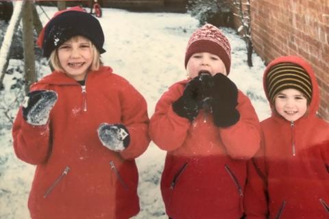 three children wearing red coats and wooly hats with snow behind them