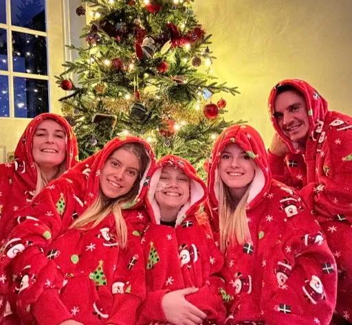 Theo and his family in matching red christmas onesies in front of a Christmas tree