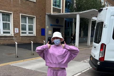 Fran posing outside the hospital wearing a face mask and pink  tracksuit