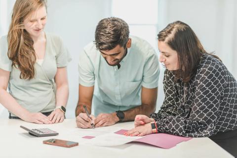 A young couple and a professional woman leaning against a table looking at and signing a document