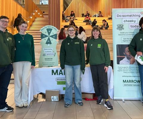 A photo of five young people wearing Anthony Nolan branded jumpers and stood in front of a donor recruitment stall at Warwick University.