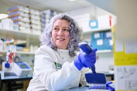 Researcher in a lab coat smiling while using a multichannel micropipette
