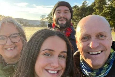 A selfie photo of the Smith family,  all beaming, in front of a blue sky and trees