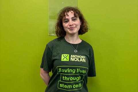 A young woman standing against a green coloured wall wearing an Anthony Nolan tshirt.