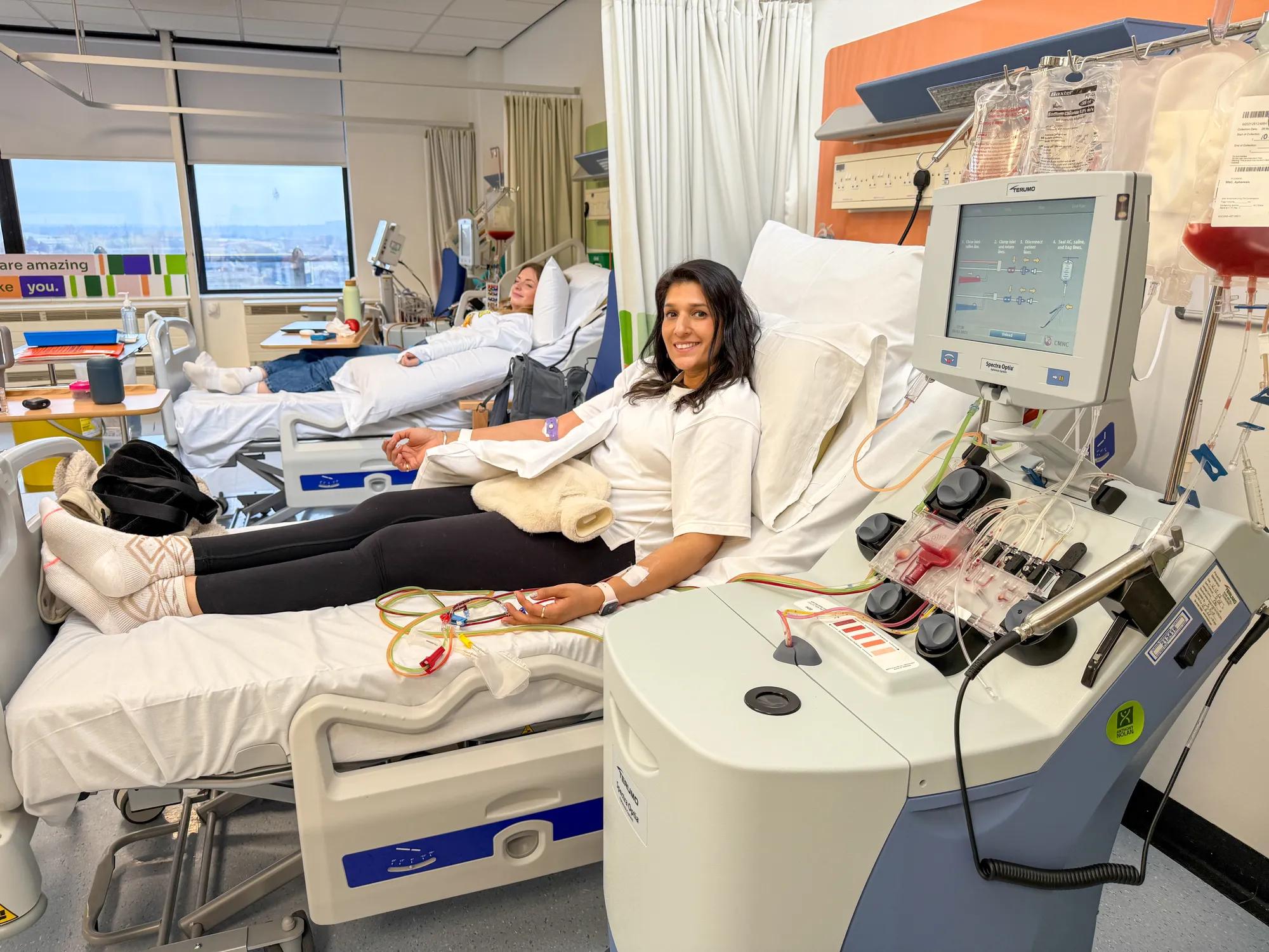 A female member of staff lying in a hospital bed donating stem cells smiling at the camera