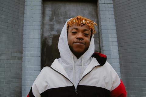 Close up of a young black male with bright orange dreads smiling with his hood up